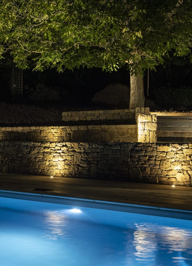 Piscine éclairée de nuit avec reflet bleu et muret en pierre