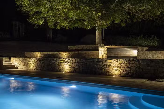 Piscine éclairée de nuit avec reflet bleu et muret en pierre