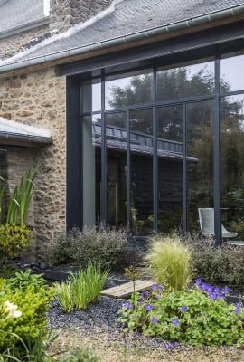 Jardin avec une maison en pierre et baie vitrée